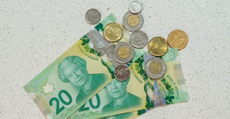 Three twenty dollar bills are on a table with a handful of coinage on top